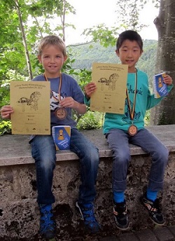 Julien und Jiaxuan auf einer Mauer mit Urkunden